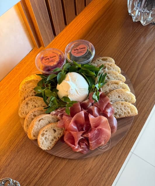 Burrata com folhas, Parma e fatias de pão em tábua redonda